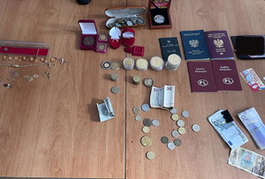 na stole leżą odzyskane przez policjantów przedmioty skradzione przez mężczyznę: dwa paszporty, monety kolekcjonerskie, dwie karty pojazdu, plik banknotów i bizuteria