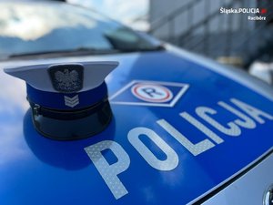 Czapka policjanta ruchu drogowego leży na masce radiowozu policyjnego. Na masce napis: policja. Nad napisem logo ruchu drogowego.