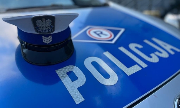 Czapka policjanta ruchu drogowego leży na masce radiowozu policyjnego. Na masce napis: policja. Nad napisem logo ruchu drogowego.