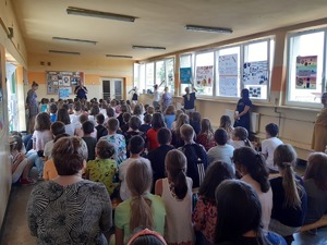 Policjant rozmawia w szkole z grupą dzieci i ich opiekunami.