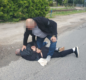 policjant w trakcie zatrzymanie mężczyzny, który leży na ziemi. Zatrzymany ma zapięte kajdanki z tyłu