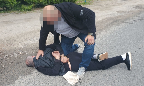 policjant w trakcie zatrzymanie mężczyzny, który leży na ziemi. Zatrzymany ma zapięte kajdanki z tyłu