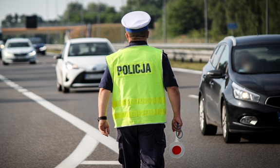 Policjant ruchu drogowego na drodze z tak zwanym lizakiem w ręku. Na drodze jadące w stronę policjanta samochody