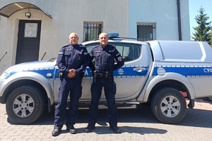 Dwaj umundurowani policjanci - aspirant sztabowy Kazimierz Kowalski i młodszy aspirant Krzysztof Kamiński stoją na tle radiowozu