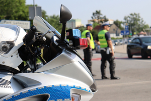 fragment policyjnego motocykla i dwaj umundurowani policjanci ruchu drogowego stojący na jezdni