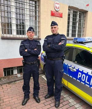 dwóch umundurowanych policjantów stojących przy radiowozie. W tle Komisariat Policji III w Sosnowcu