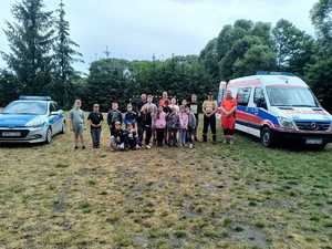 Policjant z ratownikami medycznymi pozuje do zdjęcia z grupą dzieci.