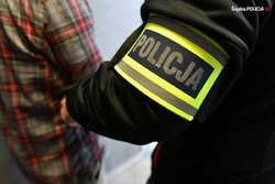 policjant prowadzi zatrzymanego - widoczna na zdjęciu opaska na ramieniu policjanta z napisem Policja