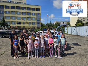 Policjantki pozują do zdjęcia z grupą dzieci za nimi stoi radiowóz policyjny.