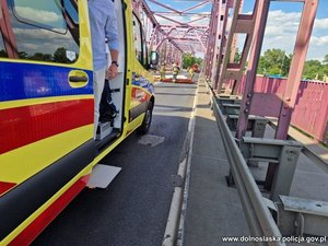 karetka pogotowia stojąca na moście, w głębi strażacy