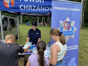 Policjantka stoi w namiocie profilaktycznym i rozdaje informatory profilaktyczne.