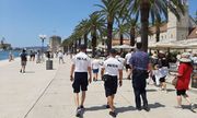 Nabrzeże portowe, z lewej zatoka, z prawej palmy, na pierwszym planie odwróceni tyłem trzej umundurowani policjanci z tego dwaj w białych koszulkach z napisem Policja. Trzeci w koszuli w kolorze niebieskim.