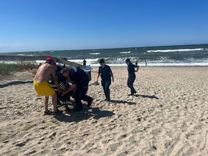 Troje policjantów pomaga mężczyźnie na wózku inwalidzkim wydostać się z plaży