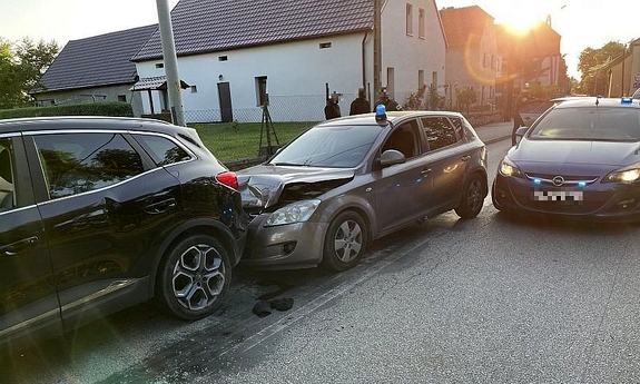 Samochód policyjny nieoznakowany po kolizji z samochodem osobowym, w dali stoją policjanci w cywilnym ubraniu