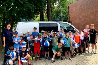 Dzieci stojące wraz z umundurowaną policjantką na tle radiowozu Policji