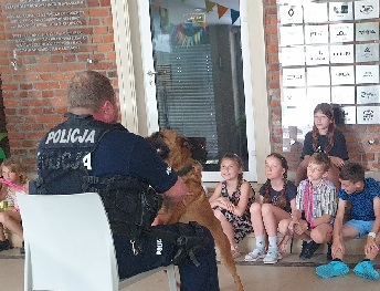 Policjant siedzący na krześle przed nim dzieci i pies służbowy