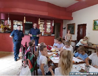Policjanci stojący przed dziećmi siedzącymi przy stołach i malujące