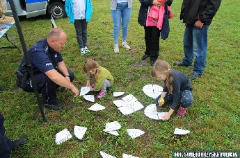Policjant w mundurze obok dzieci układających duże puzle na trawie