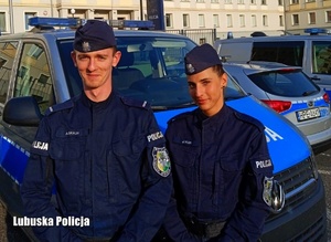 Policjant i policjantka, w tle radiowozy policyjne