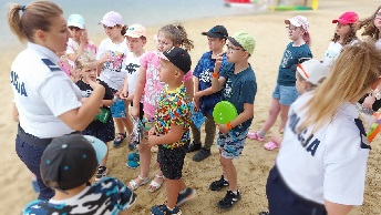 Policjantki w umundurowaniu stojące na plaży wśród grupki dzieci