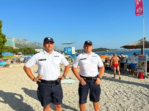 dwaj polscy policjanci stoją na plaży, w tle  wypoczywający ludzie