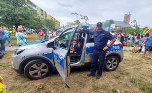Policjant stoi przy radiowozie w wewnątrz na miejscu kierowcy siedzi dziecko.