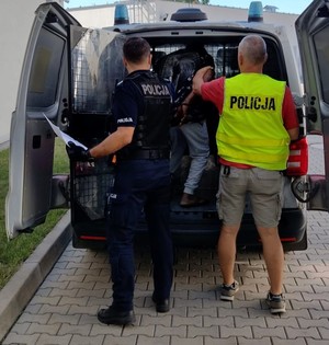 dwaj policjanci wprowadzają zatrzymanego do radiowozu policyjnego