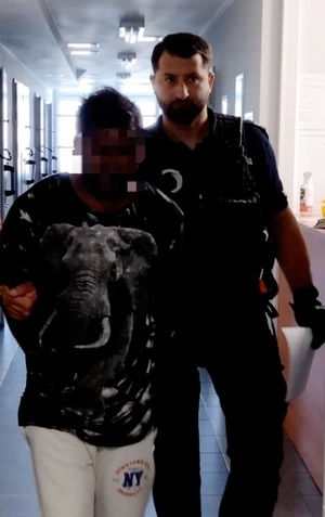 policjant prowadzi zatrzymanego mężczyznę, zakutego w kajdanki