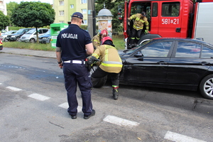 policjant stoi przy samochodzie poszkodowanego mężczyzny i strażacy pracujący przy samochodzie