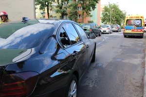 samochód poszkodowanego z widoczną wybitą szybą w tylnych drzwiach, w tle karetka pogotowia