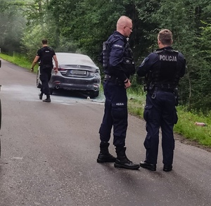 trzech policjantów na drodze w tle stoi samochód