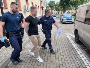 dwaj umundurowani policjanci prowadzą zatrzymanego mężczyznę