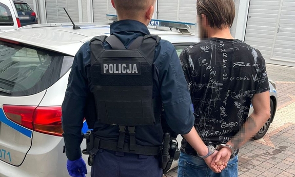 policjant z zatrzymanym mężczyzna zakutym w kajdanki przy radiowozie
