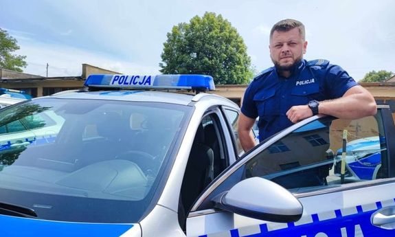 policjant w granatowym mundurze stojący za otwartymi drzwiami radiowozu