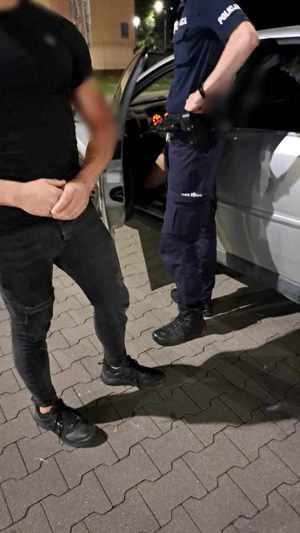 Umundurowany policjant stoi przy otwartych drzwiach auta, przy nim stoi ubrany po cywilnemu mężczyzna