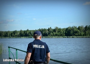 Policjant odwrócony tyłem obserwuje akwen wodny.