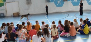 Para policjantów wraz z psem służbowym prowadzą zajęcia dla grupy dzieci.