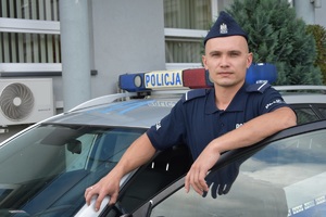 Zdjęcie kolorowe. Umundurowany policjant na tle radiowozu