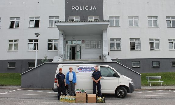 policjanci wraz z zebranymi darami na tle samochodu biorącego udział w konwoju humanitarnym