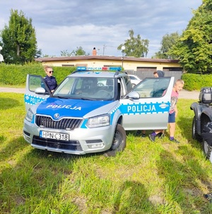Policjantka obok radiowozu wraz z uczestnikami pikniku.