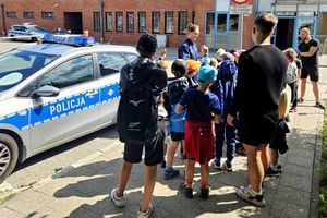 Policjantka z grupą dzieci i ich opiekunami przed budynkiem Komendy.