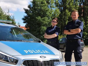 Policjantka i policjant stoją przy radiowozie