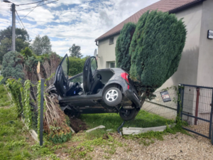 Na zdjęciu widoczny samochód osobowy, który wypadł z drogi i zawisł na ogrodzeniu posesji