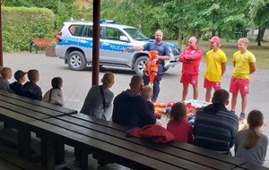 Policjant i ratownicy WOPR rozmawiają z dziećmi.
