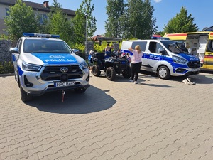 Uczestnicy pikniku przy pojazdach służbowych Policji.