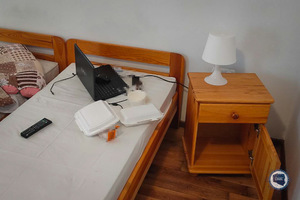 Wnętrze pokoju. Na łóżku leży laptop. Obok łózka szafka nocna a na niej lampka