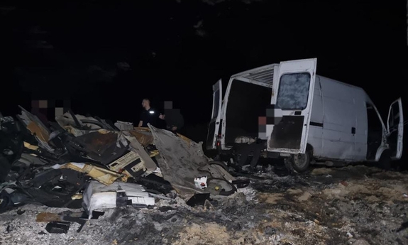biały bus z otwartymi tylnymi drzwiami, a przed nim leży wielka sterta odpadów samochodowych