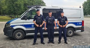 Policjanci biorący udział w akcji ratowniczej stoją przed radiowozem