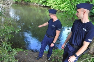 Policjant wskazuje ręką na lustro wody.