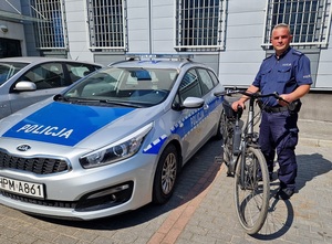 umundurowany policjant z odzyskanym rowerem, obok stroi radiowóz